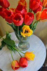 bouquet of red tulips in a glass vase on the round table beside them lay three tulips