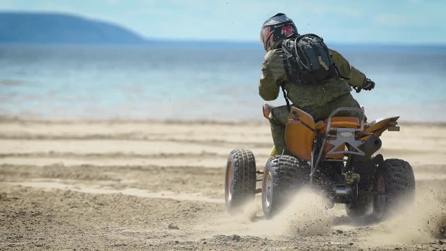 Beach. The man on the ATV. The racer does roundabouts on sand on the ATV. The peculiarity of the ATV is huge tires, high ground clearance and high power.