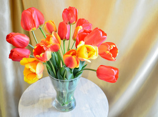 a bouquet of multicolored tulips in a glass vase on round table