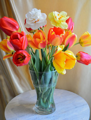 a bouquet of multicolored tulips and daffodils in a glass vase