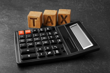 Wooden blocks with word TAX and calculator on gray background
