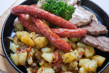 grilled sausages with potatoes, and roasted meat on a grill pan