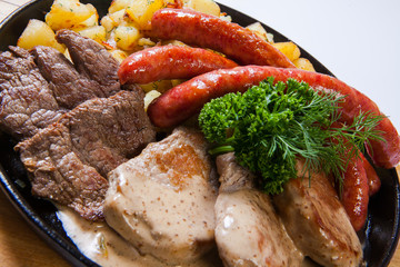 grilled sausages with potatoes, and roasted meat on a grill pan