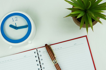 Top view of clock, plant, pen and open notebook written on white back ground.Education and business...