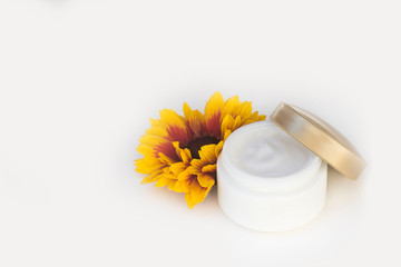 Fototapeta na wymiar Cosmetic cream container and yellow flowers on white background.