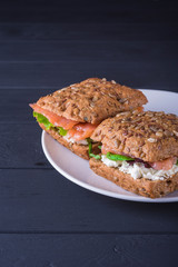 Rye sandwich with fish salmon with tomatoes and cream cheese on a plate. Wooden black background