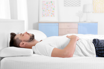 Young man lying on bed with orthopedic pillow at home