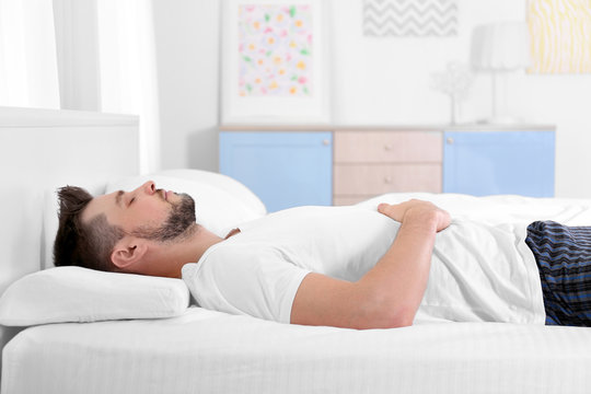 Young man lying on bed with orthopedic pillow at home