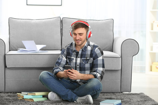 Concept of audiobook. Handsome young man with headphones and phone sitting on carpet at home
