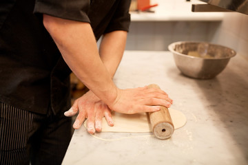 chef with rolling-pin rolling dough at kitchen