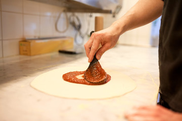 Fototapeta na wymiar cook applying tomato sauce to pizza at pizzeria