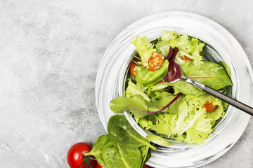 The dietary mixed greens salad (mesclun, mache, lettuce) and cherry tomatoes in a bowl on a light background. Top view, copy space. Food background