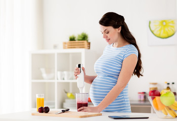 pregnant woman with blender cooking fruits at home