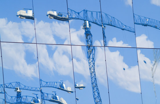 Distrorted images of construction cranes reflected in large glass windows of building