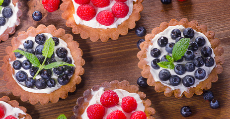 Homemade tarts with raspberries and blueberries on  wooden table.