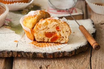 Close up of freshly baked almond and apricot muffins sprinkled with sugar powder and almond petals in a rustic setting on the decorated wooden board.