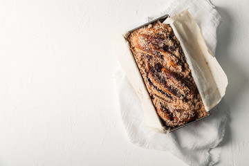 Chocolate babka in a baking tray with parchment sheet on white textured background. Homemade cocoa bun with baking utensils. Traditional french cuisine