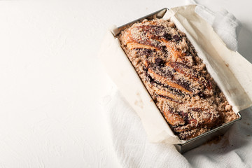 Chocolate babka in a baking tray with parchment sheet on white textured background. Homemade cocoa bun with baking utensils. Traditional french cuisine
