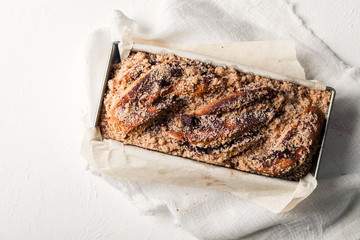 Chocolate babka in a baking tray with parchment sheet on white textured background. Homemade cocoa bun with baking utensils. Traditional french cuisine