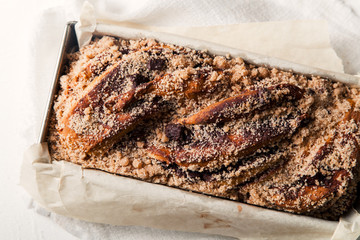 Chocolate babka in a baking tray with parchment sheet on white textured background. Homemade cocoa bun with baking utensils. Traditional french cuisine