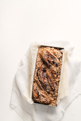 Chocolate babka in a baking tray with parchment sheet on white textured background. Homemade cocoa bun with baking utensils. Traditional french cuisine