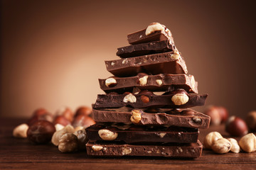 Pile of dark and milk chocolate with nuts on brown background