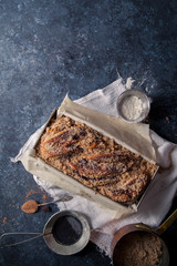 Chocolate babka on blue rustic background. Homemade cocoa bun on parchment paper with baking utensils. Traditional french cuisine