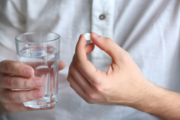 Young man with pill and glass of water, closeup