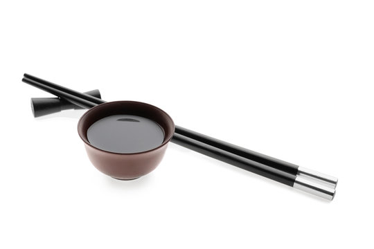 Bowl with tasty soy sauce and chopsticks on white background