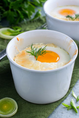Eggs baked with onions and cheese in white molds, selective focus