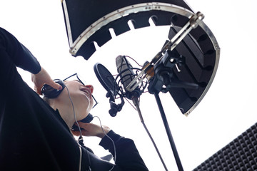 Piosenkarka śpiewa do mikrofonu podczas nagrywania utworu w studio nagraniowym.