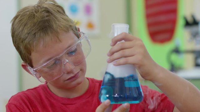 Boy in school classroom looking at bubbling science experiment