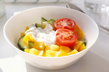 Bowl with tasty yogurt and vegetables on table, closeup