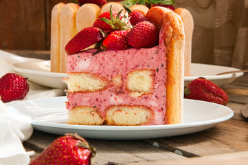 Cut of Strawberry Basil Tiramisu with fresh berries in a white plate on a wooden background....