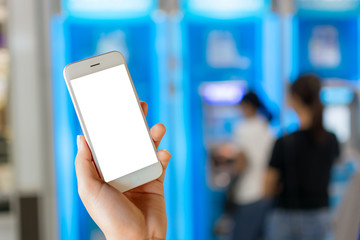 Female hand holding white phone with blank screen on blurred ATM machine background for money financial concept.