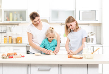 Obraz premium Young woman and her daughters cooking in kitchen