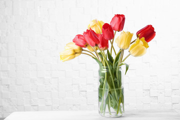 Vase with beautiful flowers on table against light background