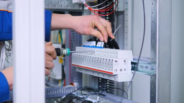 Unrecognised man fastens the connections in fuse box, electric rack. Close-up. 4K.