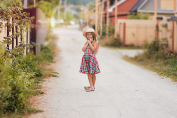 Sweet girl in retro dress and hat is walking along the village street in the summer