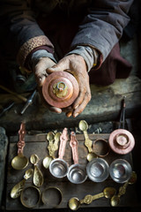 An old craftsman is holding in his hand a cup, traditional Tibetan copper handicraft product in his workshop in Chilling village in the Indian Himalaya. Chilling, Ladakh, India