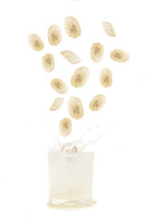 Banana slices falling into a glass of banana milkshake isolated on white