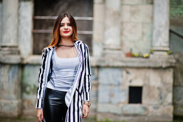 Fashionable woman look with black and white striped suit jacket, leather pants,  posing at old street. Concept of fashion girl.