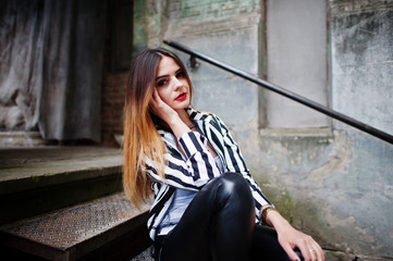 Fashionable woman look with black and white striped suit jacket, leather pants, posing at old street on iron stairs. Concept of fashion girl.