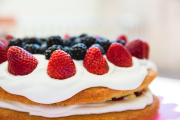 Light sponge cake with white icing and mixed berries (strawberries, blackberries, blueberries) on top. Bright light, warm perfect for summer.