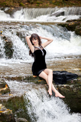 Portrait of a brunette in a black dress near a mountain river. The model is posing at the waterfall.