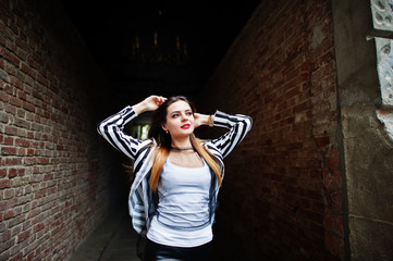 Fototapeta premium Fashionable woman look with black and white striped suit jacket, leather pants, posing at old street red brick tunnel. Concept of fashion girl.