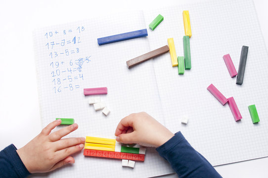 Open exercise book with colored plastic math learning tools number rods on white background. Close-up of children's hands. solving mathematics examples. Educational and school concept.