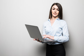 Attractive young girl in casual clothes is holding a laptop, looking at camera and smiling, on gray background