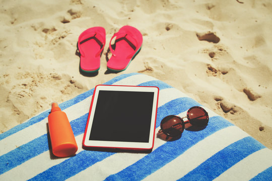 Suncream, flip-flops and touch pad on beach