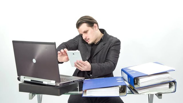 A busy worker is multitasking. He is talking on one phone, swiping on the other and also working on his computer.